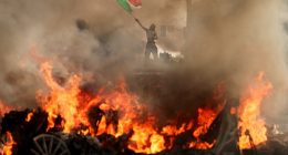 Images of the violence showse a man waving a Mexican flag as flames rise from a burning Waymo