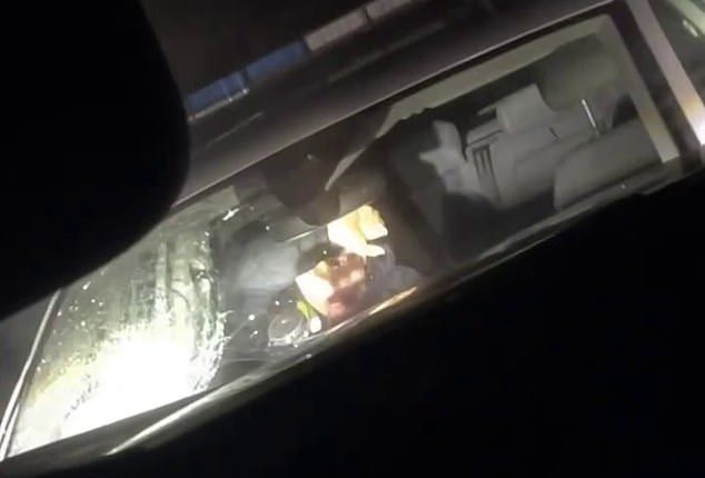 Pictured is the moment a female officer ducked for cover after a large stone was lobbed at the windshield of a parked police vehicle