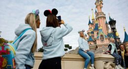 Welcome to the warped world of the Disney Adult – a world into which Wolfe delves in her new book that she says is part celebration of her 'tribe,' part cautionary tale. (Pictured: A woman has her picture taken in front of the castle in Disneyland Paris in 2023)